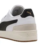 Championes Puma modelo Shuffle Downtown OG, de diseño urbano con base blanca, detalles en negro y suela de goma color caramelo. Presentan refuerzos en gamuza gris en la puntera y el talón, con el logo de la marca en dorado.
