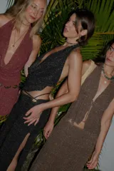 Falda larga tejida color marrón con brillo metálico, corte al cuerpo, abertura alta en la pierna y recortes laterales con cordones ajustables.