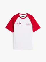 Remera de cuello redondo con diseño de mangas raglán en color rojo y cuerpo en color blanco. Presenta un estampado gráfico en el pecho con banderas de carreras y el logo de la colaboración Tommy Hilfiger x Cadillac Formula 1 Team.