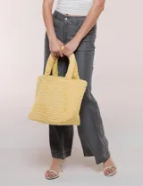 Cartera tipo shopper color amarillo de textura soft y flexible, con doble asa superior fija y compartimento principal amplio con botón metálico.