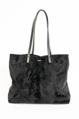 Bolso tipo tote de gran tamaño en color negro con acabado aterciopelado. Cuenta con doble asa larga para llevar al hombro y placa metálica decorativa en la parte frontal.