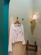 Blusa blanca de encaje con cuello en V, mangas largas acampanadas y lazo ajustable en el frente.