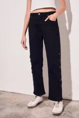 Pantalón de jean negro, de corte recto y tiro medio. Presenta bolsillos delanteros y traseros, y una hilera de botones metálicos a lo largo de la costura lateral.