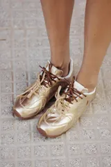 Zapatillas de cuero color dorado brillante, con cordones marrones y cordones transparentes intercambiables. Suela de goma color caramelo.