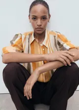 Camisa de lyocell con estampado de rayas verticales en tonos naranja, marrón y beige. Tiene cuello camisero, manga larga con puños abotonados y cierre frontal con botones.