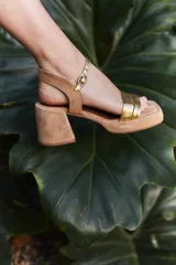 Sandalias de taco cuadrado medio, con base y talón en gamuza color tostado. Presenta una tira frontal de múltiples bandas doradas y una pulsera al tobillo con hebilla metálica.
