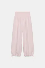 Pantalón baggy de tiro medio color rosado, con cintura elástica fruncida tipo nido de abeja y bajos ajustables con cordones.
