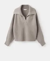 Jersey de punto color beige, con cuello polo, escote en V y mangas largas con puños ajustados. Presenta una textura acanalada y un diseño holgado.