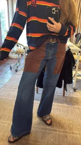 Pantalón de jean de corte recto y tiro medio, con paneles frontales de cuero marrón que simulan una chaparrera. Incluye un falso cinturón de cuero integrado con hebilla metálica.