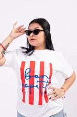 Remera oversize blanca de algodón suave con cuello redondo, con un estampado central que combina franjas verticales rojas y la frase 'bon appétit!' escrita en azul con tipografía cursiva.