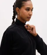 Campera deportiva de mujer confeccionada en tejido plush aterciopelado. Presenta cuello alto, cierre frontal con cremallera y puños ajustados.