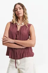 Blusa sin mangas color gris claro con textura rayada vertical y lazo ajustable en el escote.