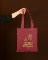 Tote bag de tela en color bordó con estampado gráfico en color amarillo que representa una fogata y una persona sentada, junto con la frase 'Invierno Uruguayo' y 'Charlas Largas & Risas Estufa'.