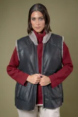 Chaleco reversible de cuero negro con interior de piel sintética gris. Presenta cierre frontal completo y bolsillos laterales con cierre.