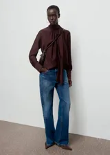 Blusa de cuello alto con detalle de fular integrado, confeccionada en tejido con textura. Presenta diseño recto, manga larga con puños abotonados y cierre posterior.