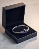 Pulsera de plata con diseño trenzado y una piedra circonia redonda facetada en color azul zafiro en el centro.