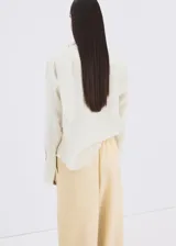 Blusa de modal y poliéster color blanco marfil, con diseño recto, escote en V, mangas largas y detalle de fular incorporado en el cuello. Cierre frontal con botones.
