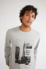 Remera de manga larga color gris melange, con cuello redondo y estampado gráfico en blanco y negro de la ciudad de Nueva York en el frente.