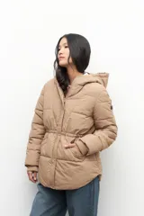 Campera puffer color tostado con capucha, cierre frontal con botones a presión y bolsillos laterales. Presenta diseño acolchado, puños elásticos y ajuste en la cintura.