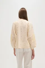 Blusa de viscosa color blanco con diseño holgado, cuello en V y cierre frontal con botones. Presenta detalles de bordado tipo broderie en el frente y en las mangas abullonadas.