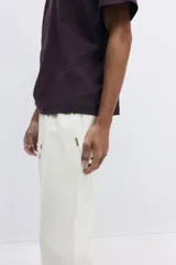 Jogger color blanco hueso en tejido suave de mezcla de algodón, con pliegue cosido en la parte delantera. Presenta cierre decorativo, cintura elástica con cordón ajustable, bolsillos laterales y un bolsillo insertado en la parte trasera. Corte estándar.