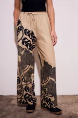 Pantalón de lino color beige con estampado de hojas negras, corte flare y tiro alto.