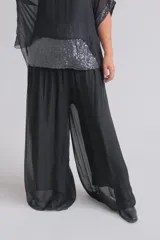 Pantalón de corte amplio y fluido, confeccionado en tela semitransparente color negro, con cintura elástica y diseño de pierna ancha.