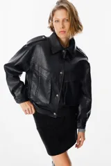 Chaqueta de cuero sintético negro con textura granulada, corte oversize, cuello camisero, cierre frontal con botones a presión, bolsillos frontales con solapa y charreteras en los hombros.