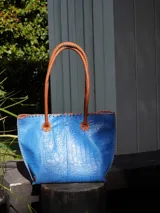 Bolso shopper de cuero azul con textura crocco, manijas largas marrones y costuras artesanales visibles en los bordes.