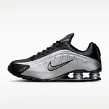 Championes Nike modelo Shox R4, con diseño futurista que combina paneles de cuero sintético negro y plateado metálico. Presenta la icónica tecnología de amortiguación Shox en el talón con columnas plateadas y el logo de Nike en el lateral.