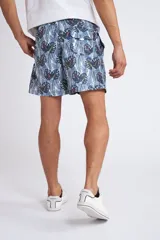 Short de baño con cintura elástica y cordón ajustable, confeccionado en tela ligera de secado rápido. Presenta un estampado botánico integral en tonos amarillos, blancos y azules, con dos bolsillos delanteros y uno posterior.