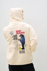 Canguro beige con capucha, cordones ajustables y bolsillo tipo canguro. Estampado en el pecho con el logo de DTMF y en la espalda con un diseño alusivo al álbum "Un Verano Sin Ti" de Bad Bunny.