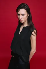 Blusa sin mangas color negro, de silueta fluida, con cuello redondo, detalle de alforzas en el frente y abotonadura parcial con botones visibles.