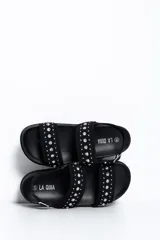 Sandalia chunky de plataforma color negro, con diseño de doble tira ancha decorada con tachas metálicas cónicas y pulsera ajustable al tobillo con hebilla.