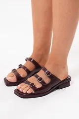 Sandalias de cuero bordó con diseño de tres tiras con hebillas metálicas regulables, punta cuadrada y taco bajo.