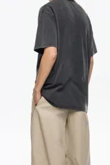 Camiseta de algodón orgánico color negro con efecto gastado, corte oversize y manga corta ancha. Presenta un estampado artístico enmarcado con el texto "BIMBA Y LOLA" en la parte superior e inferior.