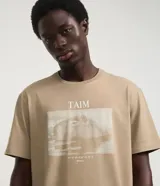 Remera de manga corta color beige claro, con cuello redondo y estampa rectangular frontal con un carpincho en el agua.