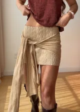 Mini falda de punto color marrón con textura tejida, diseño ajustado y detalle de lazo lateral largo que cae sobre la pierna.