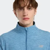 Buzo deportivo New Balance de manga larga, color celeste jaspeado (space dye), con cuello alto y cierre frontal de un cuarto. Presenta el logo de New Balance en el pecho.