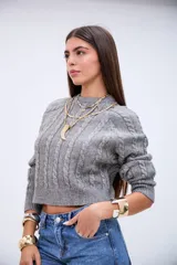 Sweater de punto gris con diseño de trenzas verticales, cuello redondo y corte cropped.