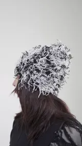 Gorro tipo beanie con diseño de hilos entrelazados en colores blanco y negro, creando un efecto visual texturizado y desmechado.
