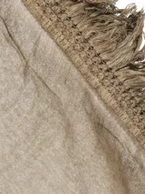 Pañuelo fino de tejido ligero, color gris, con flecos largos y densos en los bordes laterales y flecos más cortos en los bordes superiores e inferiores.