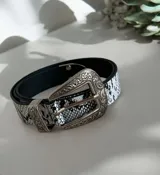 Cinto con estampado de piel de serpiente en blanco y negro, con hebilla metálica grande de estilo western con detalles grabados.