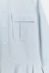 Vestido corto tipo camisero de algodón, con cuello solapa, mangas tres cuartos y cierre frontal con botones. Presenta bolsillos de plastrón con solapa en el pecho y falda con bajo plisado.