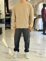 Buzo oversize de tejido waffle en color beige, con cuello redondo y manga larga, con pequeña etiqueta de marca en el dobladillo inferior.