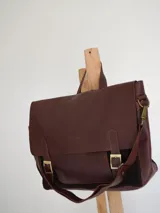 Maletín tipo cartero con solapa de cuero marrón y cuerpo de gamuza azul. Cuenta con correas ajustables con hebillas metálicas, asa superior y correa larga para llevar al hombro.