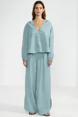 Camisa celeste de lino italiano, con silueta relajada, mangas largas, cierre frontal con botones y detalle de charm floral en el primer botón.