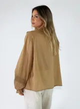 Blusa de algodón blanca con escote en V, mangas largas amplias y detalles de volados con encaje bordado en el frente.