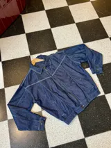 Campera de denim azul oscuro con costuras a contratono, cierre frontal, cuello clásico, bolsillos laterales y puños abotonados.