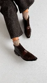 Bota corta de cuero con textura tipo reptil y paneles de gamuza en tono marrón oscuro. Presenta un diseño de punta cuadrada, cierre lateral y un taco cuadrado de madera.